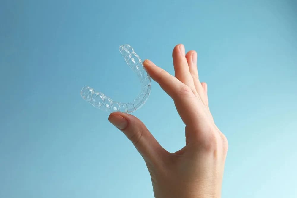 Clear aligners held by a hand against a blue backg