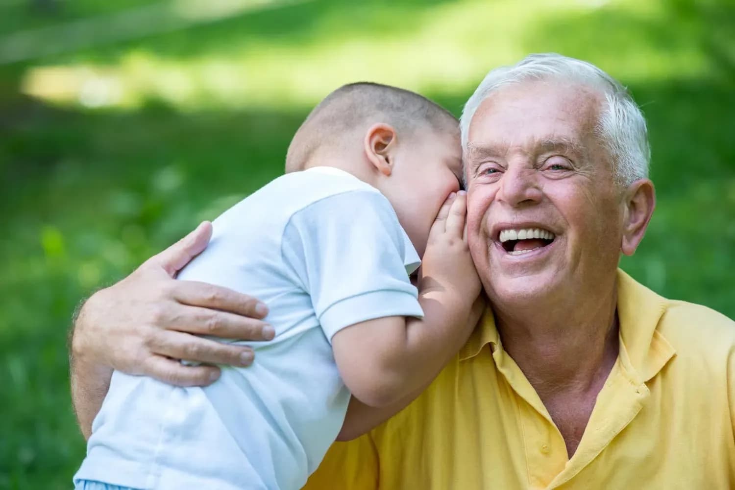 Happy grandfather with grandson sharing a secret outdoors