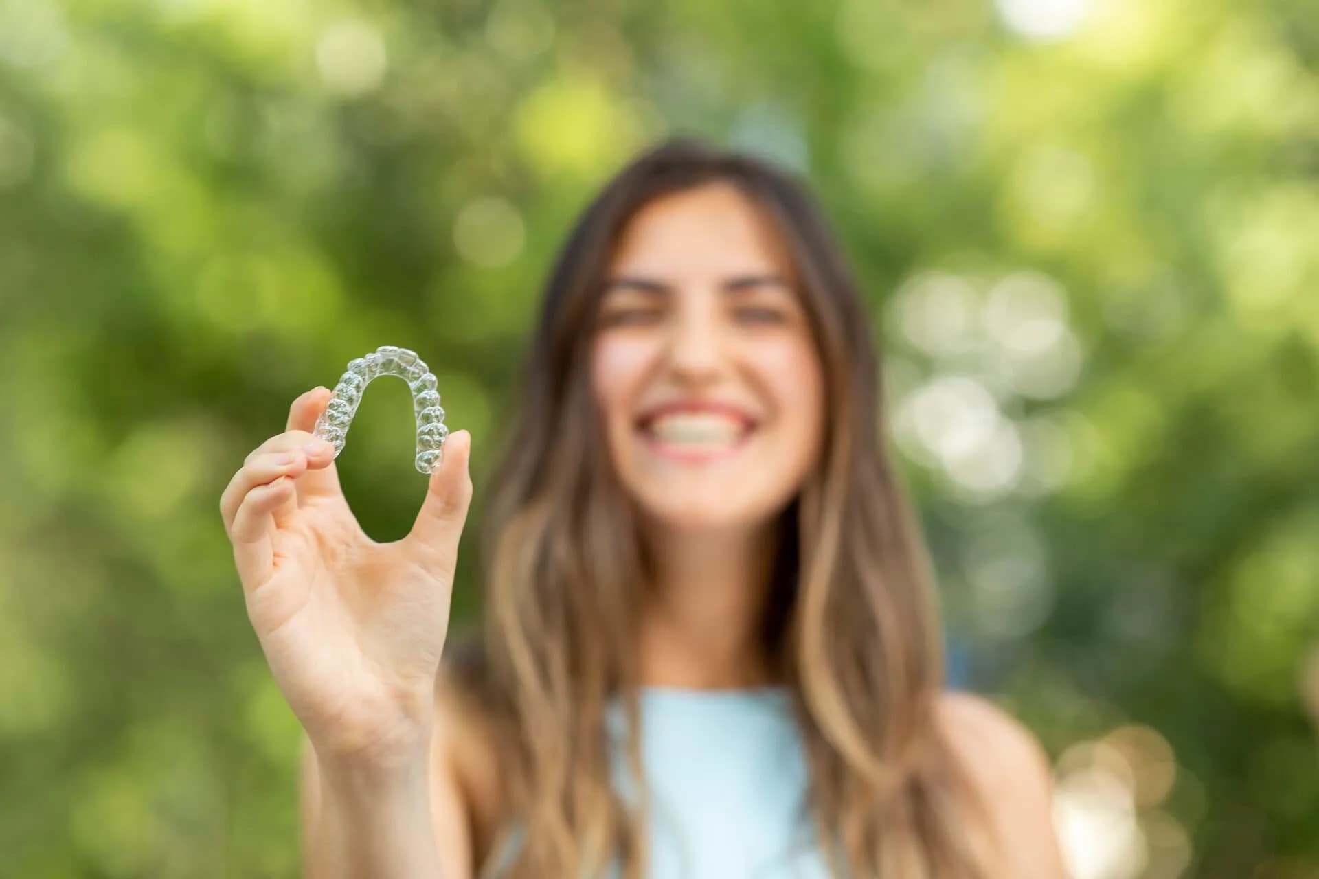 Smiling woman holding an Invisalign clear aligner at Neola Dental in Minneola, FL