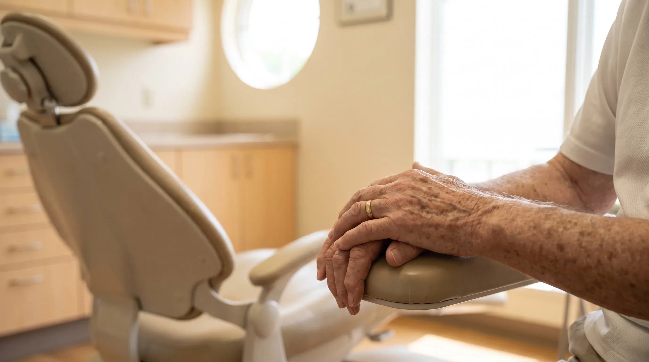 Older adult's hands resting on the armrest of a dental chair